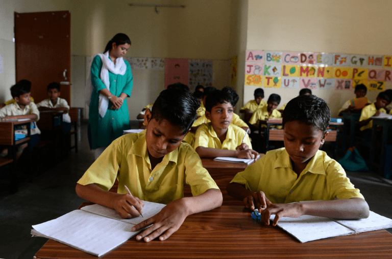 Students writing a leave letter to class teacher in classroom with guidance from teacher