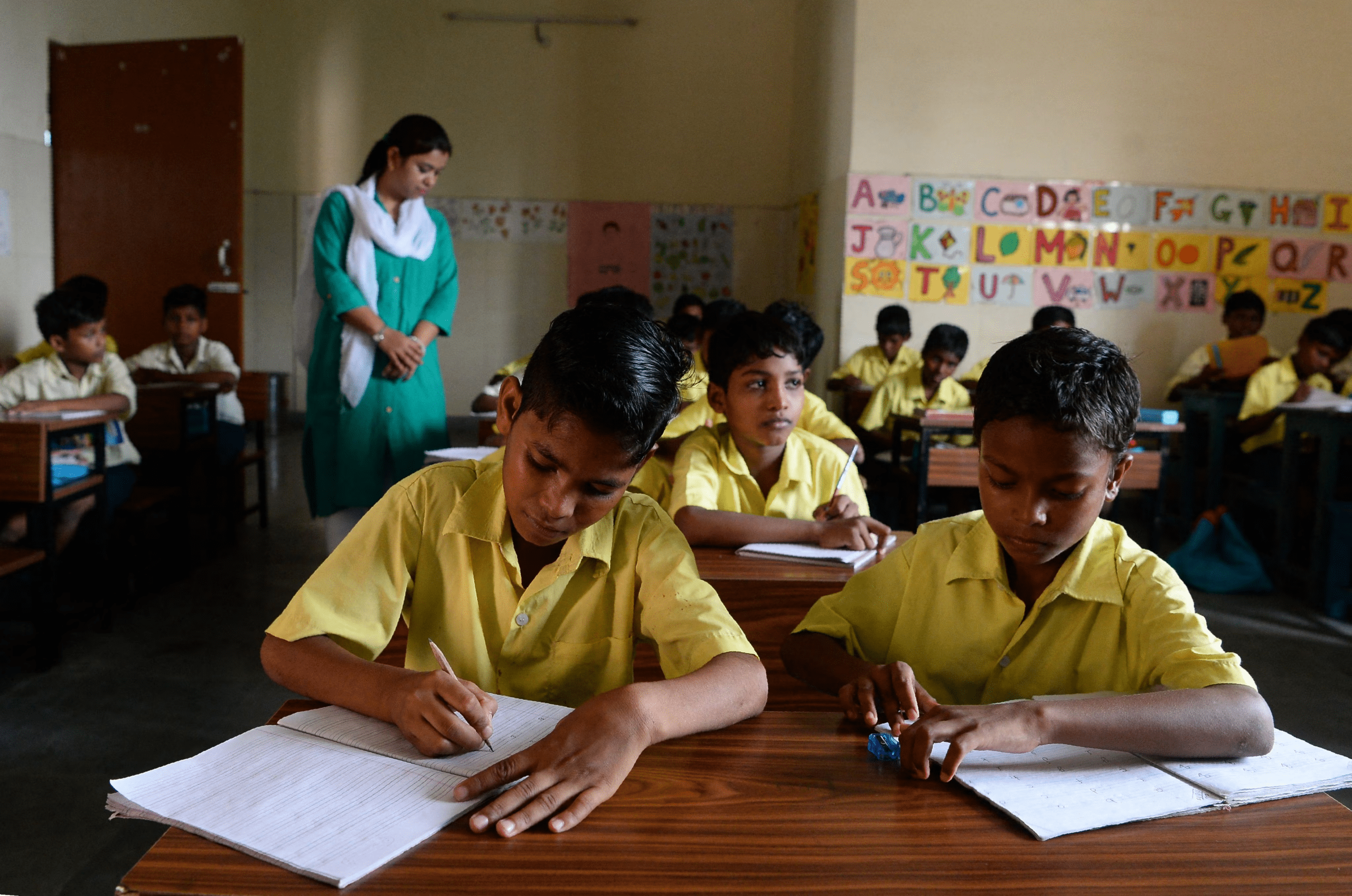 Students writing a leave letter to class teacher in classroom with guidance from teacher