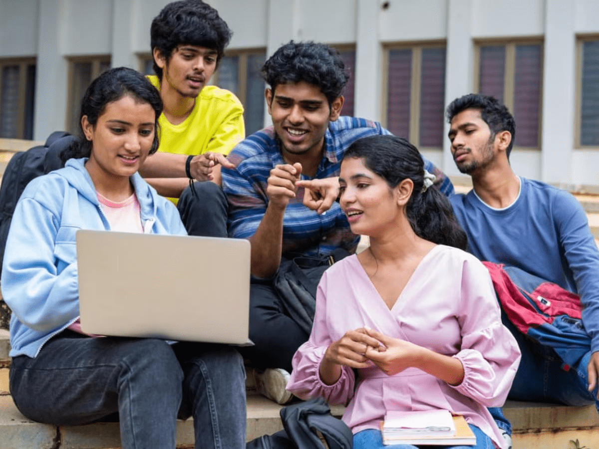 Group of Indian college students discussing together around laptop sharing motivation and success energy